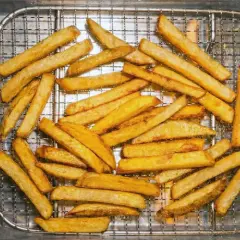 En hög med gyllene, krispiga pommes frites ligger på ett galler i en plåt. Perfekt för en snabb aptitretare.