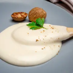 Krämig bechamelsås på en tallrik med muskotnötter och persilja. Perfekt för ditt bechamelsås recept.