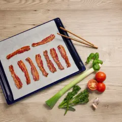 Krispigt bacon i ugn på bakplåtspapper, redo att serveras med färska grönsaker.
