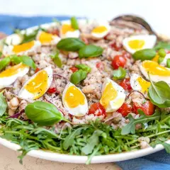 En härlig tonfisk sallad med kokta ägg, tomater, bönor och färsk basilika, serverad på en bädd av rucola.