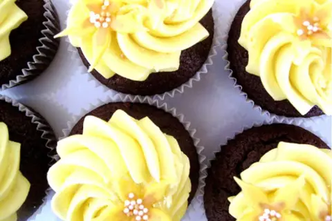 Chokladmuffins med gul frosting och blomsterdekoration. En härlig syn av frosting muffins som ser aptitliga ut.