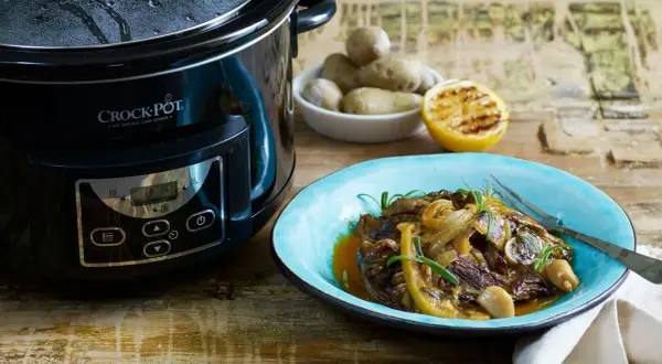 En läcker slow cooker recept med mört kött, citron och rosmarin på en blå tallrik bredvid en Crock-Pot.