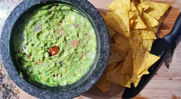Färdiggjord guacamole i en mortel, redo att serveras med tortillachips. Ett enkelt guacamole recept för alla.