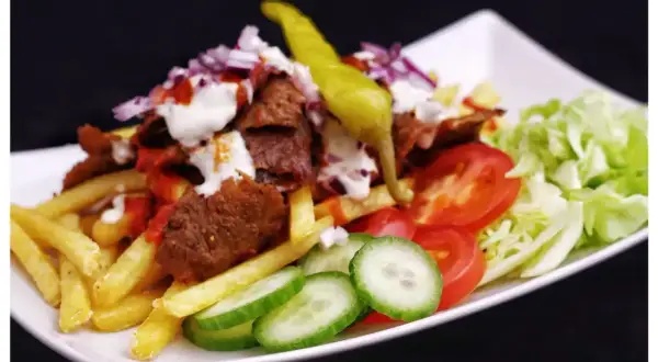 En tallrik med kebab, pommes frites, tomater, gurka, sallad och en stark chili. Perfekt för dig som söker ett gott kebabsås recept.