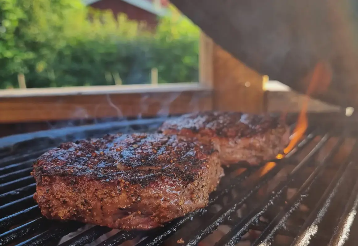 Två saftiga biffar med kryddor grillas över glödande kol. Perfekt för en sommarfest, undrar vad man kan grilla mer?