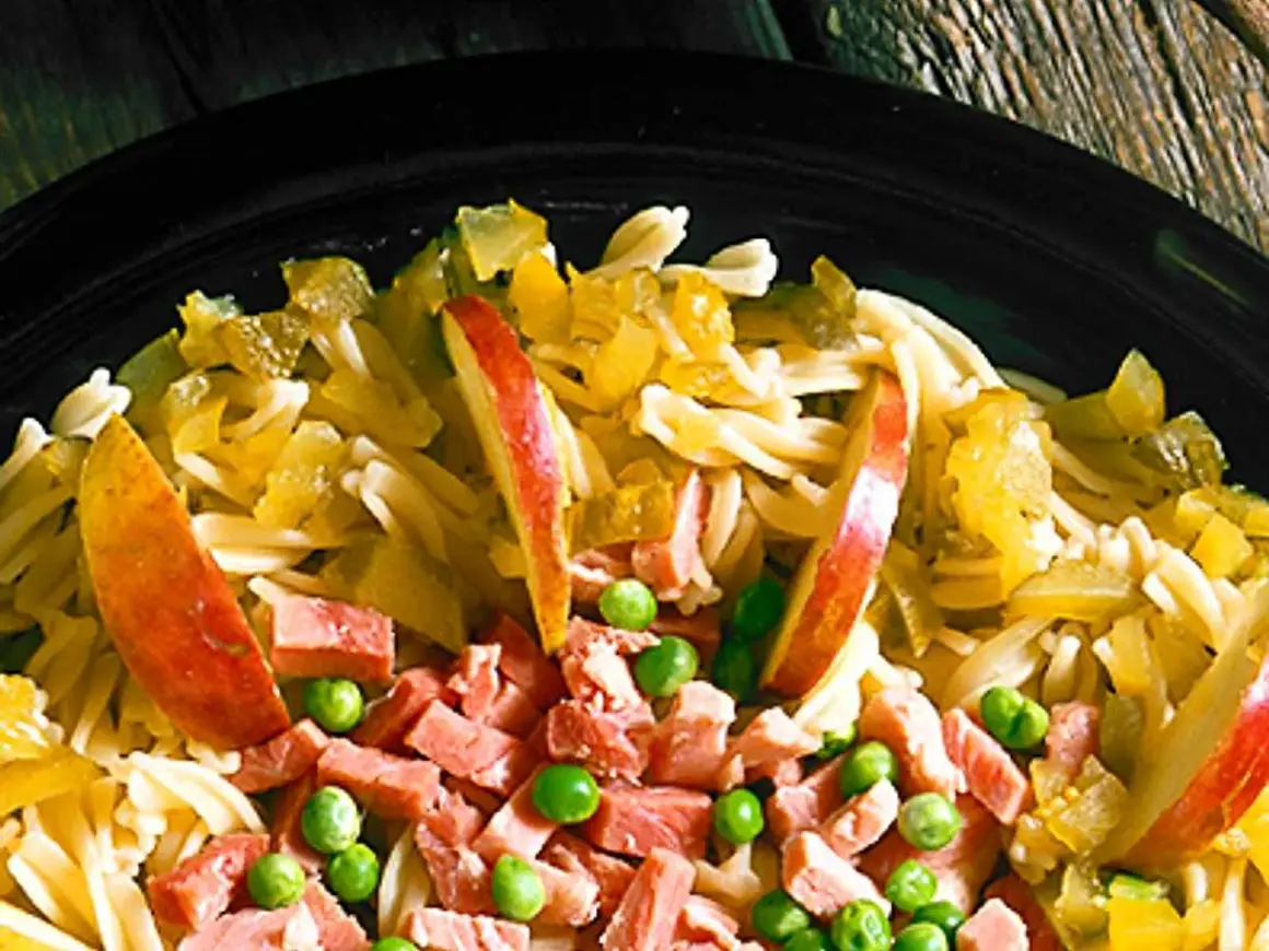 En närbild på en läcker pastasallad med skinka, äppelklyftor och gröna ärtor. En perfekt sommarmåltid!