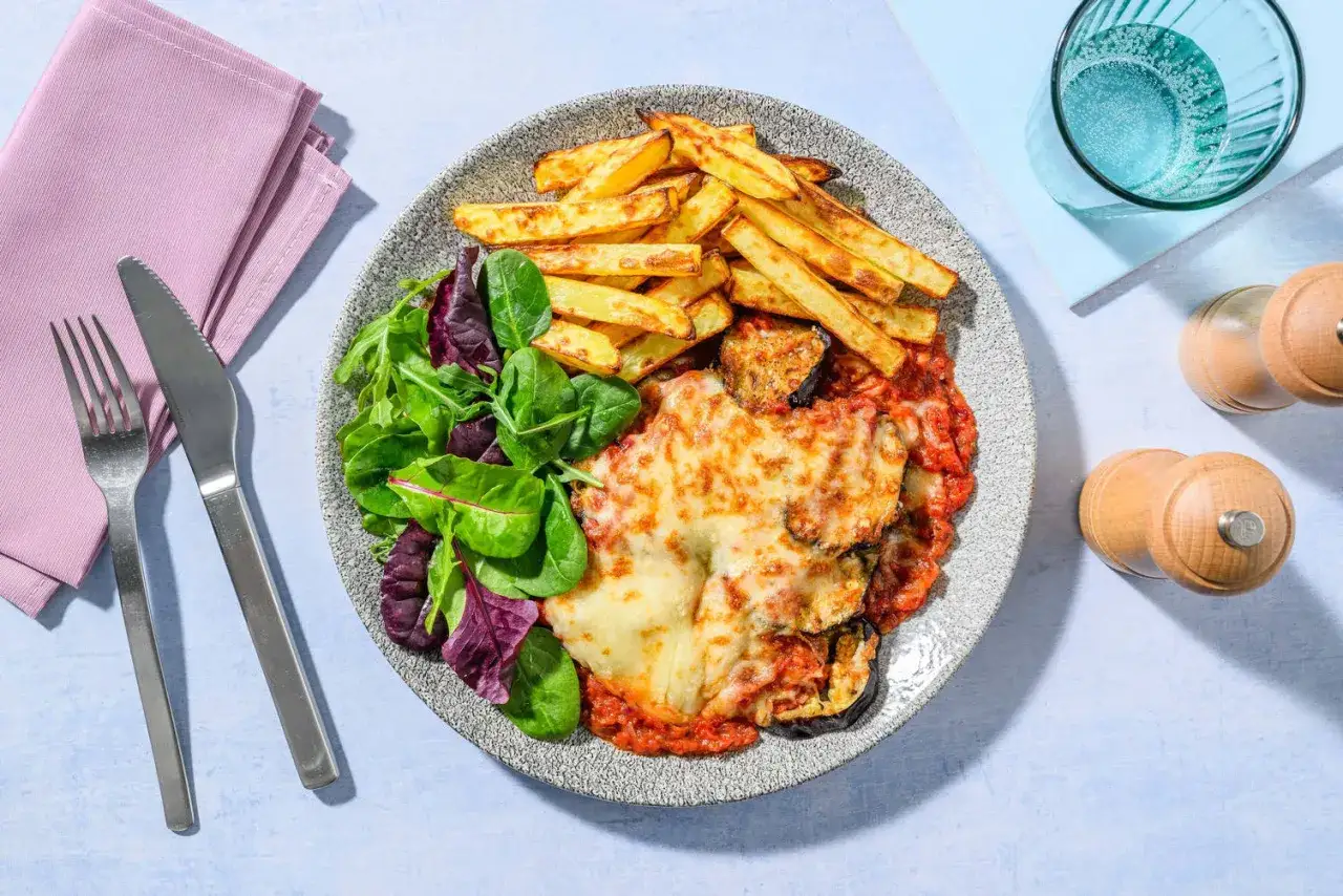 En tallrik med aubergineparmigiana, en fr&auml;sch sallad och gyllene pommes frites. Perfekt f&ouml;r en mysig middag.
