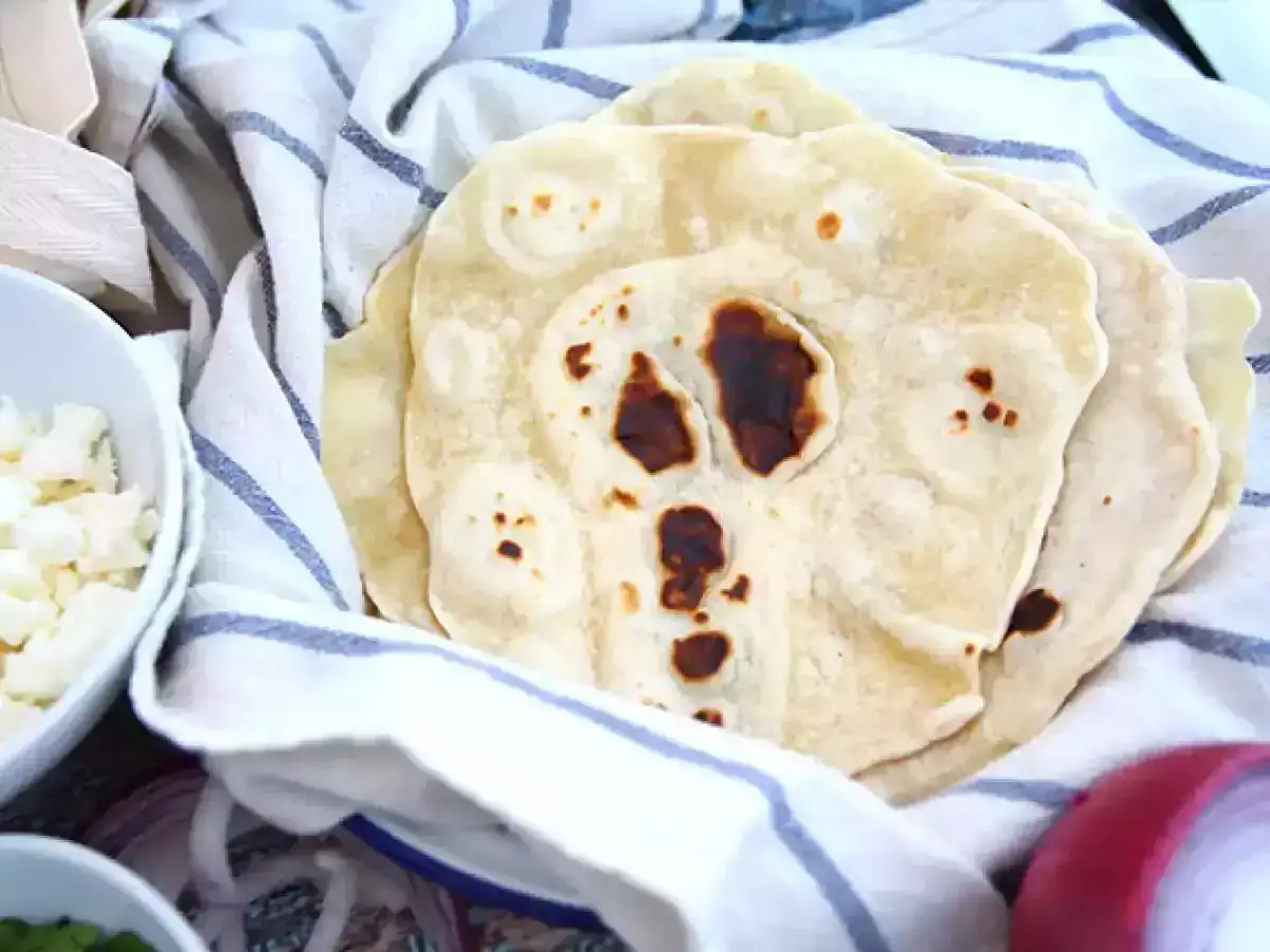 Nybakade tortillas p&aring; en randig handduk, redo f&ouml;r ditt b&auml;sta tortilla recept. Bredvid syns ost och l&ouml;k.