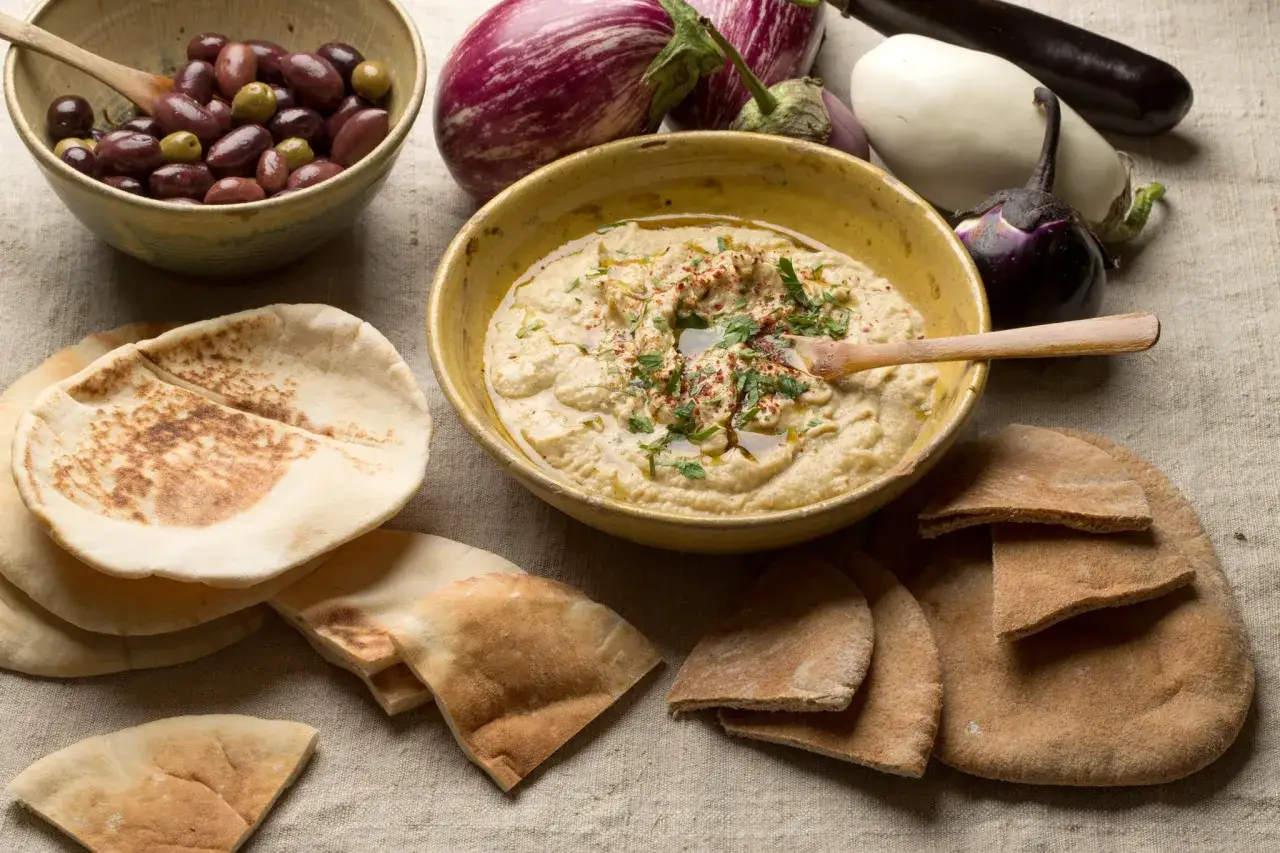 En sk&aring;l med kr&auml;mig baba ganoush, pitabr&ouml;d, oliver och auberginer. Perfekt f&ouml;r ett baba ganoush recept.