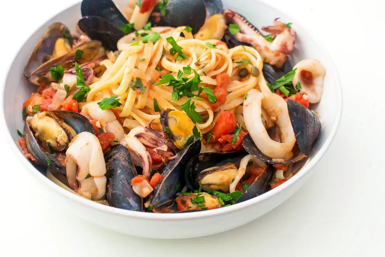 En sk&aring;l med pasta och frutti di mare, fylld med musslor, bl&auml;ckfiskringar och en tomatbaserad s&aring;s, toppad med f&auml;rsk persilja.