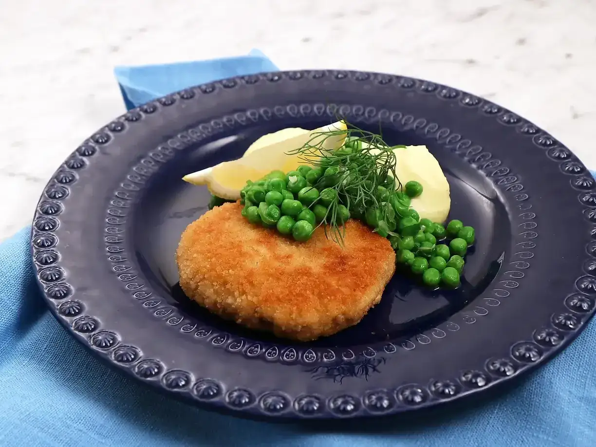 En gyllene havets wallenbergare serveras med potatis, gröna ärtor och dill på en mörkblå tallrik.