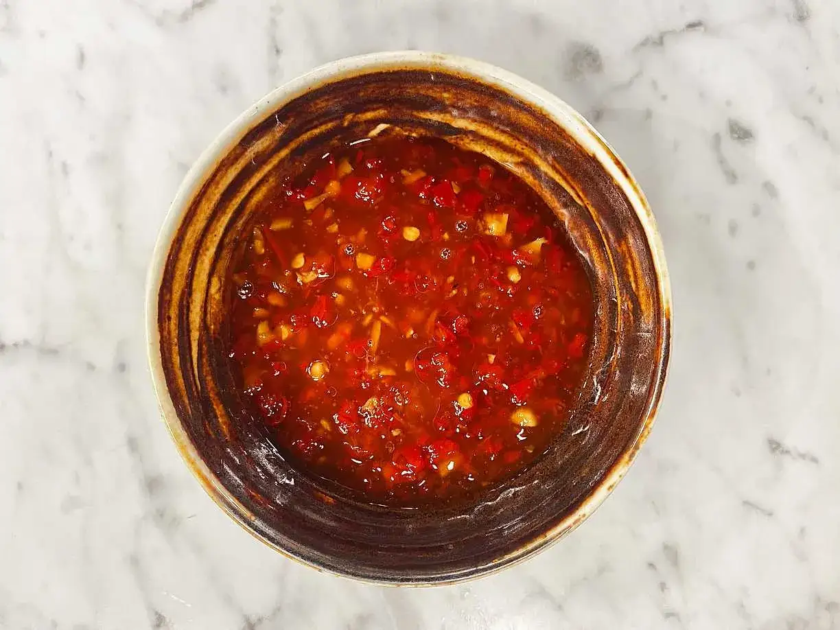 En skål med härlig, röd sweet chili sås med små bitar av chili och vitlök. Perfekt till vårrullar eller kyckling.