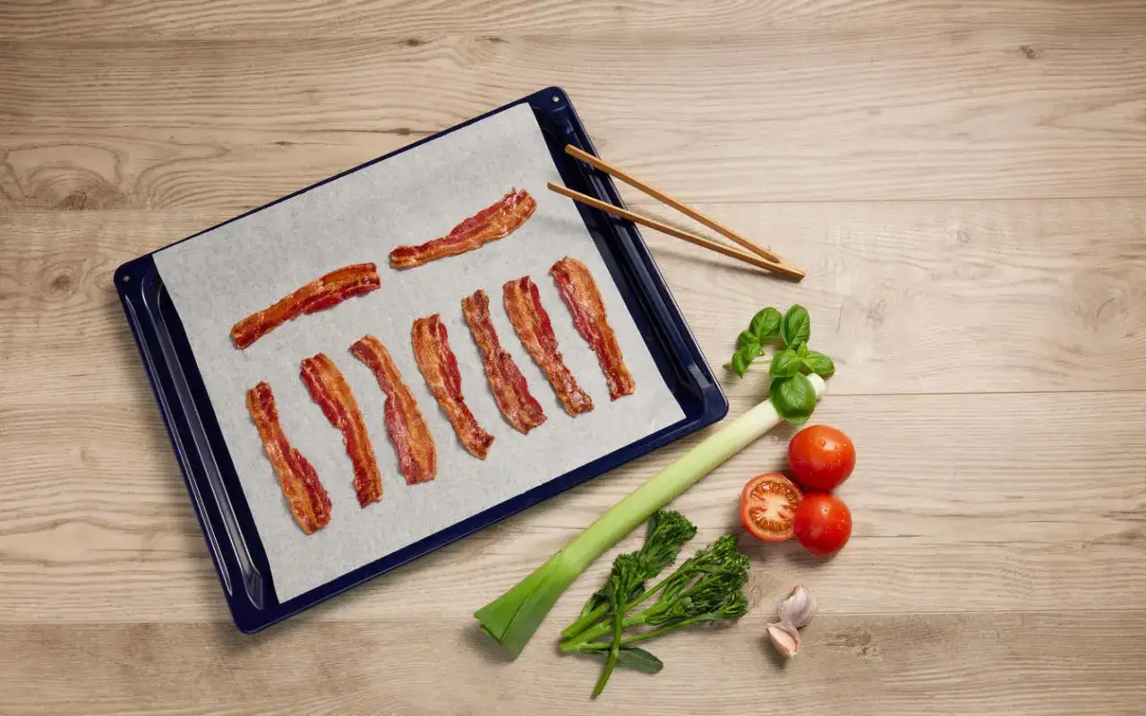 Krispigt bacon i ugn på en plåt, redo att serveras med färska grönsaker.