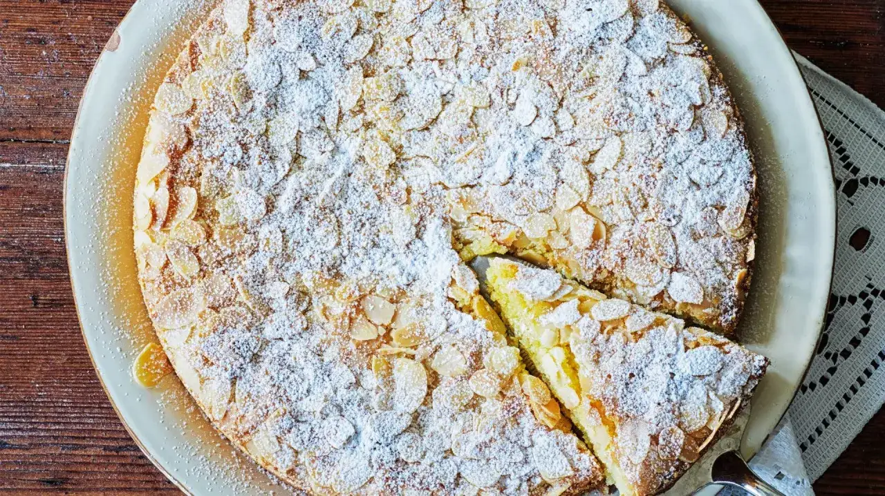 En saftig mandelkaka med citron, toppad med mandelsp&aring;n och pudersocker. En bit &auml;r uppskuren.