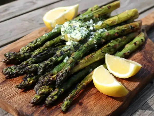 Grilla sparris med smör och dill, serverad med citronklyftor på en träbricka. Perfekt sommarbuffé!