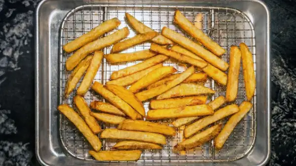 En hög med gyllene, krispiga pommes frites ligger på ett galler i en plåt. Perfekt för en snabb aptitretare.