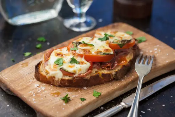 En härlig tallrik med varma mackor, toppad med smält ost, tomater och färska örter. Serveras på en träskärbräda med bestick.