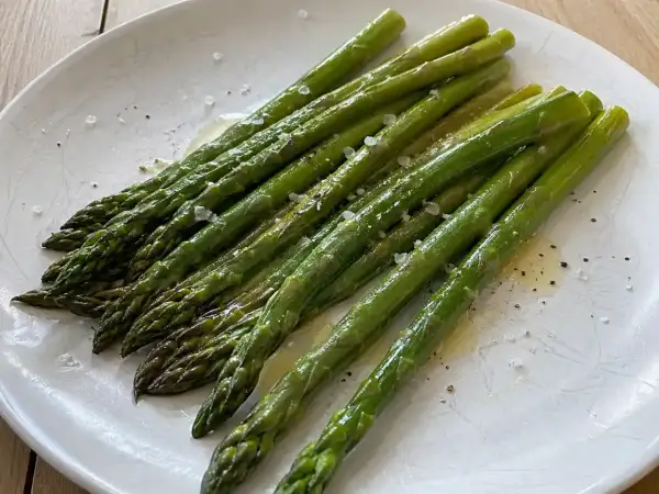 När man ska koka sparris är det viktigt att den blir perfekt. Här ligger en vackert grön, nykokt sparris på ett fat, strödd med flingsalt och peppar.